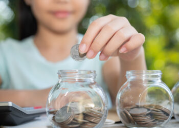 Seorang anak sedang menabung dengan memasukkan koin ke dalam jar, cara yang efektif untuk menabung cepat untuk beli HP.