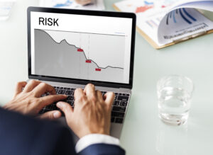 Seorang pria mengetik di laptop yang menampilkan grafik penurunan risiko dan kerugian investasi.
