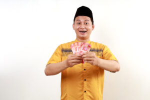 Pria muslim muda tampak gembira sambil memegang uang kertas rupiah.