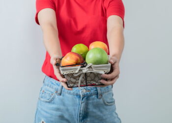 Seorang pria berkaos merah sedang memegang keranjang berisi buah