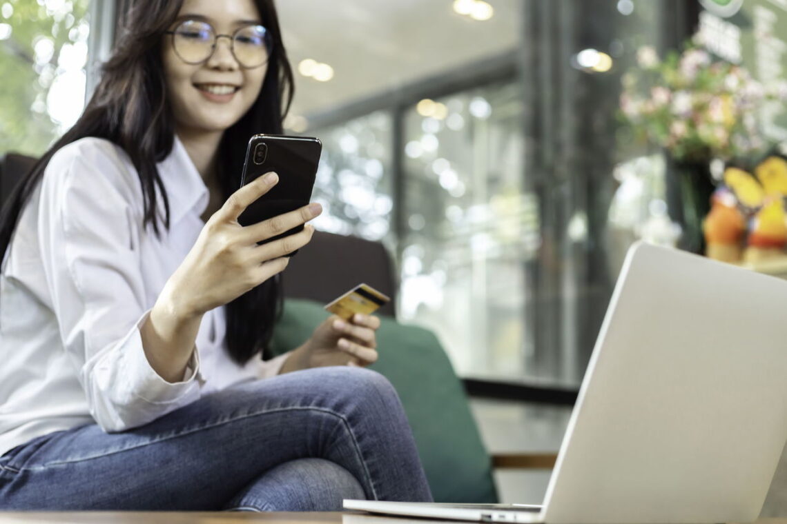 gambar seorang wanita melihat ke arah smartphone nya dan sedang memegang kartu atm