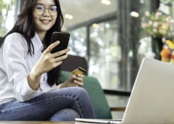 gambar seorang wanita melihat ke arah smartphone nya dan sedang memegang kartu atm