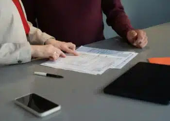 Dua orang memeriksa lembaran formulir di atas meja, ponsel dan tablet di dekatnya