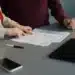 Dua orang memeriksa lembaran formulir di atas meja, ponsel dan tablet di dekatnya