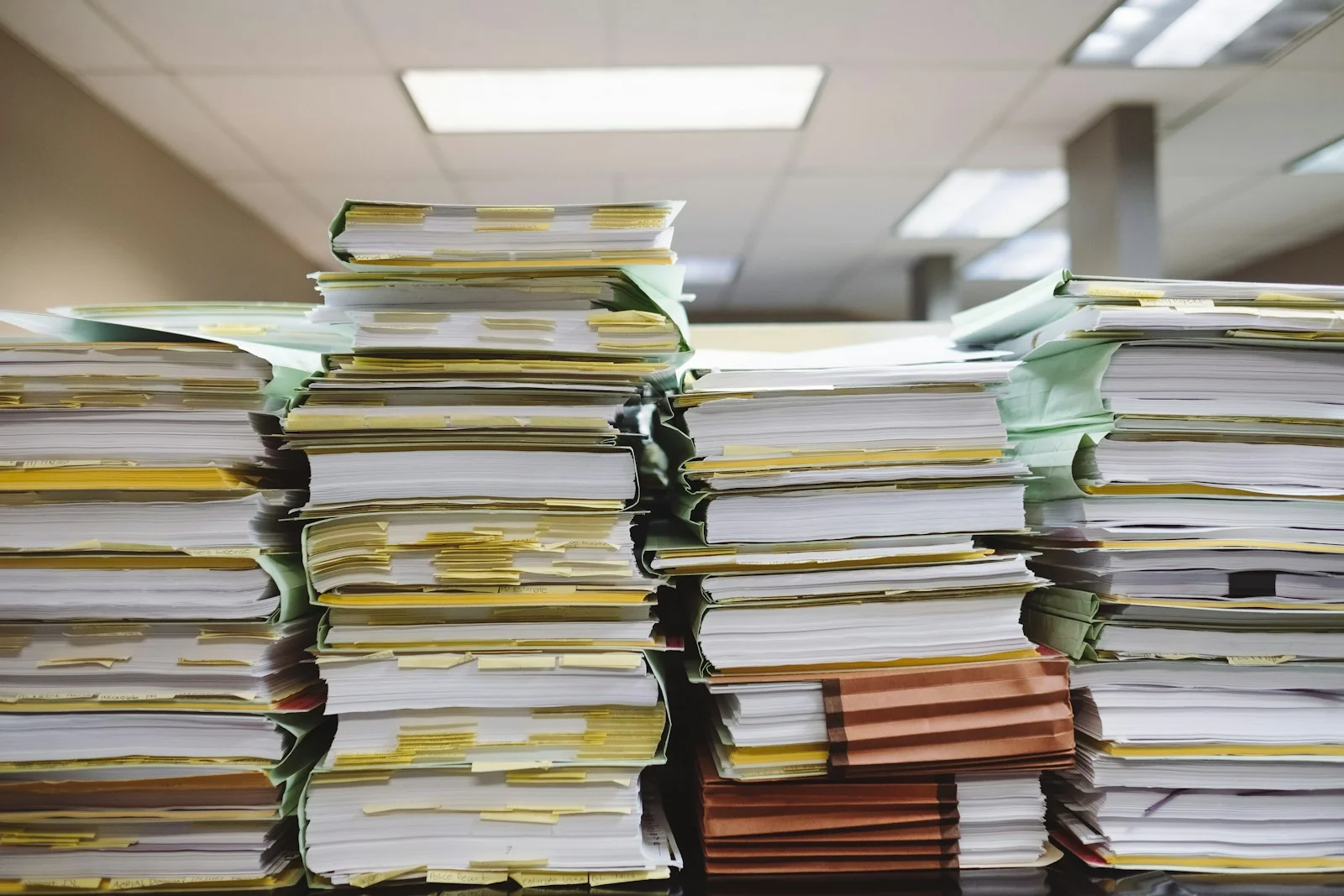 Tumpukan tinggi berkas kertas dan map dokumen bertanda di ruang kantor