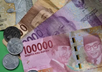 Uang kertas rupiah pecahan 100.000, 10.000, 5.000, dan 2.000 bersama koin rupiah di atas latar hijau