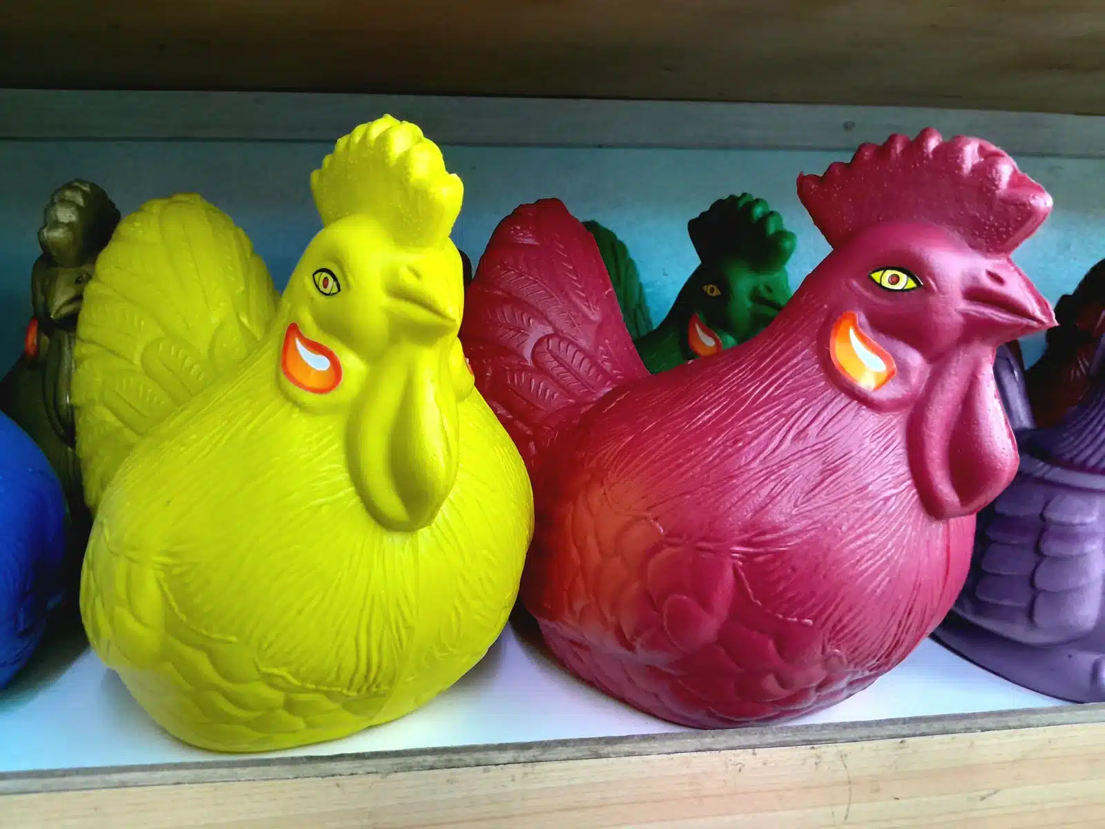 Deretan celengan ayam plastik warna kuning, merah, hijau, dan ungu di rak kayu