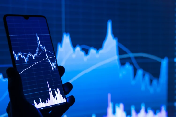 Ponsel dengan aplikasi saham di depan layar grafik