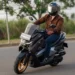 Pengendara skuter matik Yamaha berhelm full face dan jaket melaju di jalan aspal