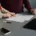 Dua orang memeriksa lembaran formulir di atas meja, ponsel dan tablet di dekatnya