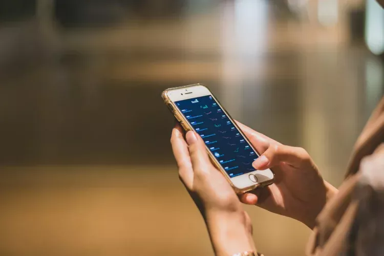 Tangan memegang ponsel yang menampilkan aplikasi keuangan