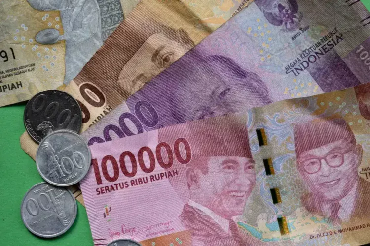 Uang kertas rupiah pecahan 100.000, 10.000, 5.000, dan 2.000 bersama koin rupiah di atas latar hijau
