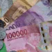Uang kertas rupiah pecahan 100.000, 10.000, 5.000, dan 2.000 bersama koin rupiah di atas latar hijau