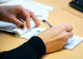 Tangan menulis di lembar buku cek dengan pena di atas meja kantor