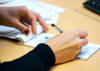 Tangan menulis di lembar buku cek dengan pena di atas meja kantor