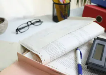 Lembar cetakan angka keuangan, map, pena, kalkulator, dan kacamata di atas meja kerja