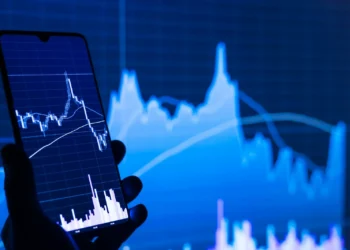 Ponsel dengan aplikasi saham di depan layar grafik