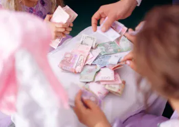 Tangan orang dewasa dan anak memilah uang kertas di atas meja