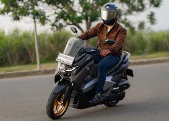 Pengendara skuter matik Yamaha berhelm full face dan jaket melaju di jalan aspal