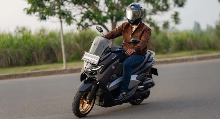 Pengendara skuter matik Yamaha berhelm full face dan jaket melaju di jalan aspal