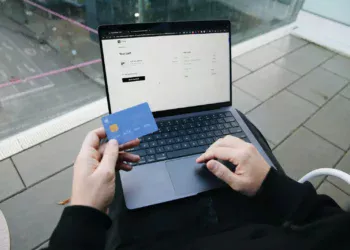 Orang duduk dengan laptop sambil memegang kartu kredit