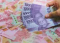 Tumpukan uang rupiah dan tangan memegang pecahan Rp10.000