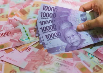 Tumpukan uang rupiah dan tangan memegang pecahan Rp10.000